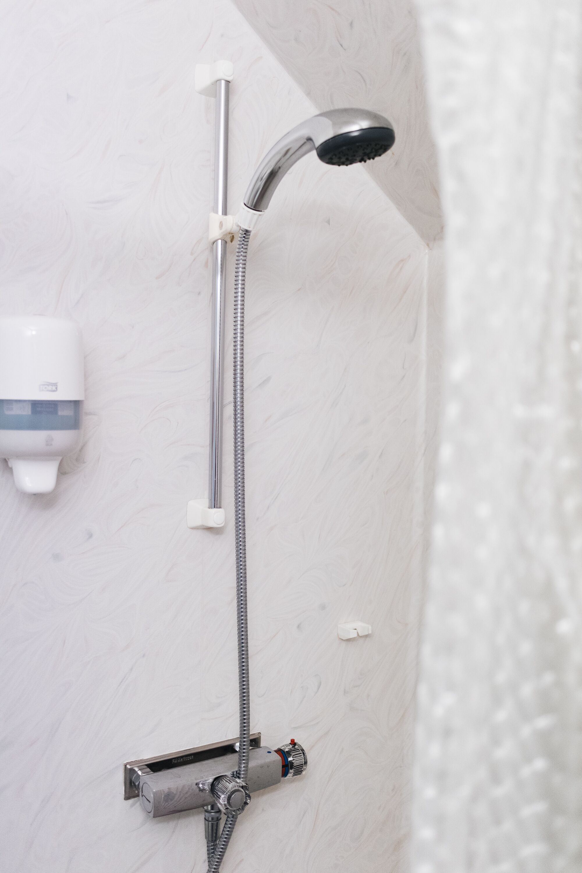 A shower with a handheld showerhead, a wall-mounted soap dispenser, and a control panel.
