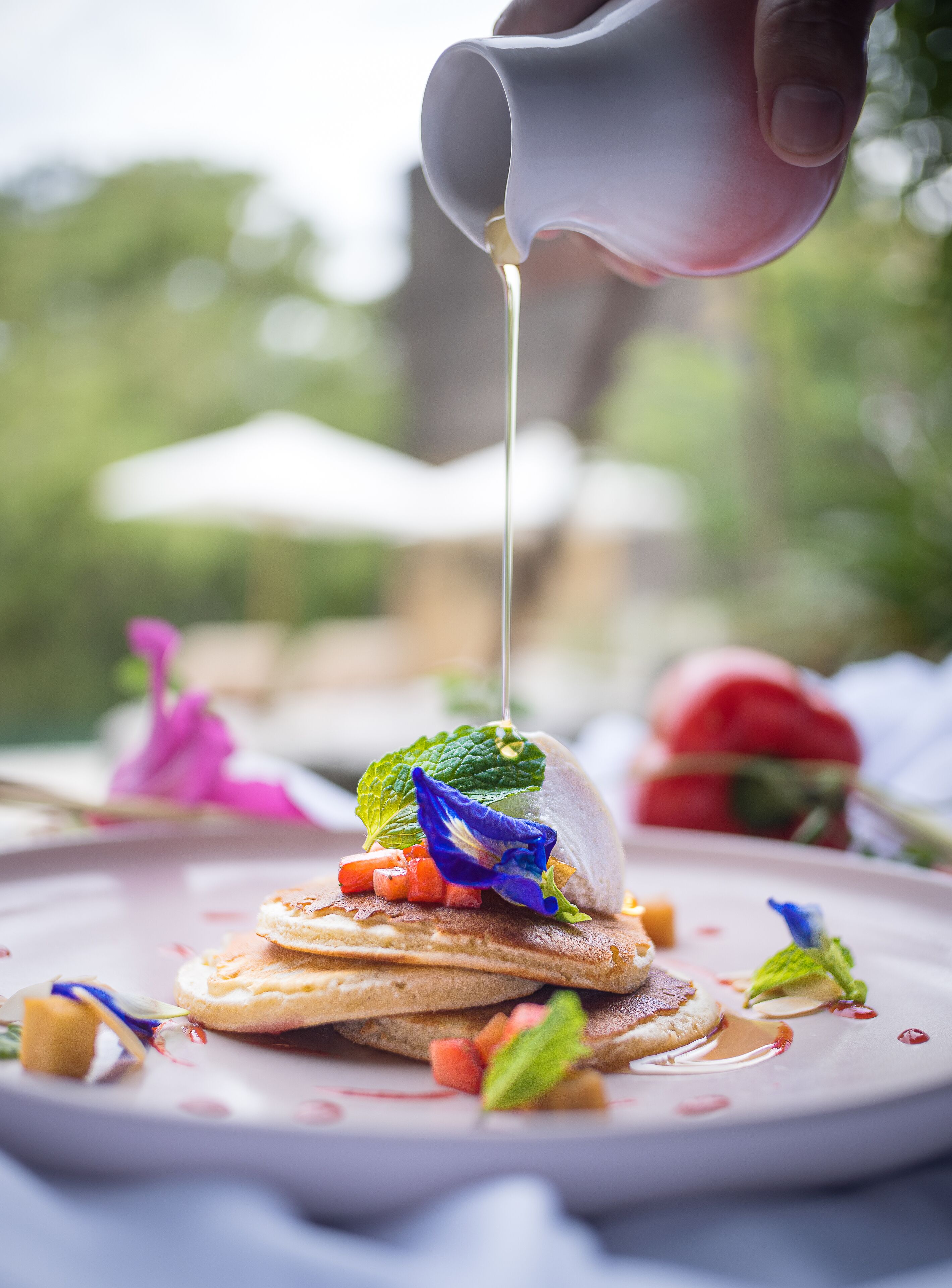 A dessert with a sauce being poured over it, garnished with mint leaves and berries, on a plate with a blurred outdoor background.