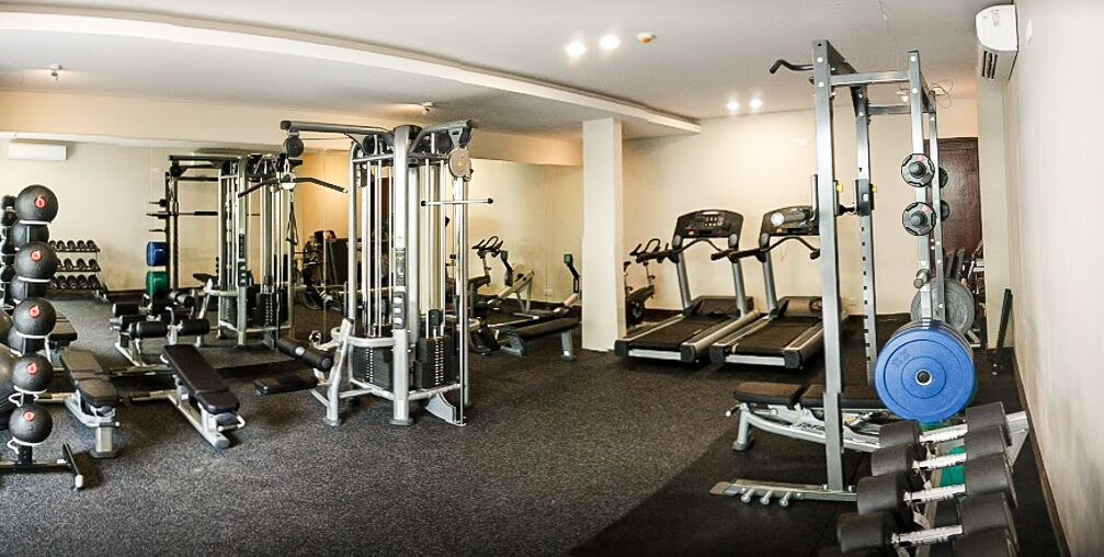 Uma academia com diversos equipamentos de ginástica, incluindo esteiras, máquinas de musculação e pesos livres.