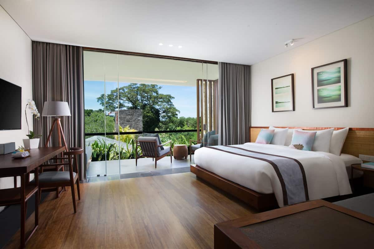 Une chambre d’hôtel moderne dotée d’un grand lit, d’un bureau et d’un balcon offrant une vue sur les arbres.