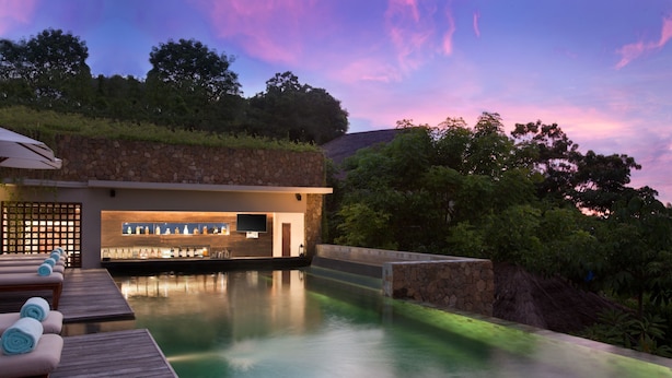 A pool area with lounge chairs and a bar, surrounded by greenery and a stone wall. - The Tamarind Resort Nusa Lembongan Bali (Lembongan Island)