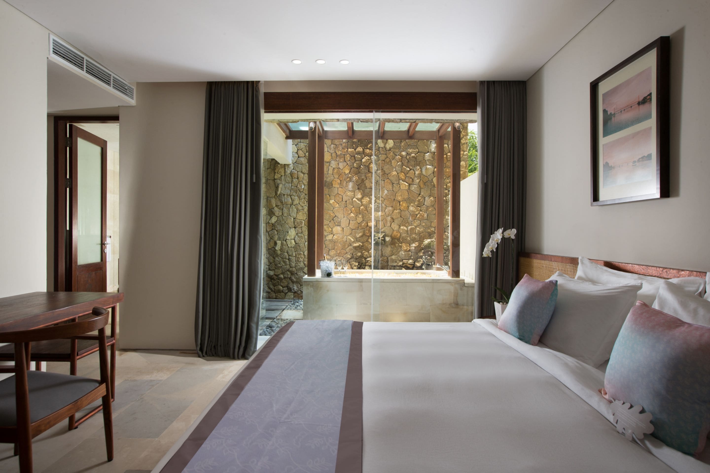 Habitación de hotel con una cama grande, un escritorio de madera, una pared de piedra y vistas a un jardín.