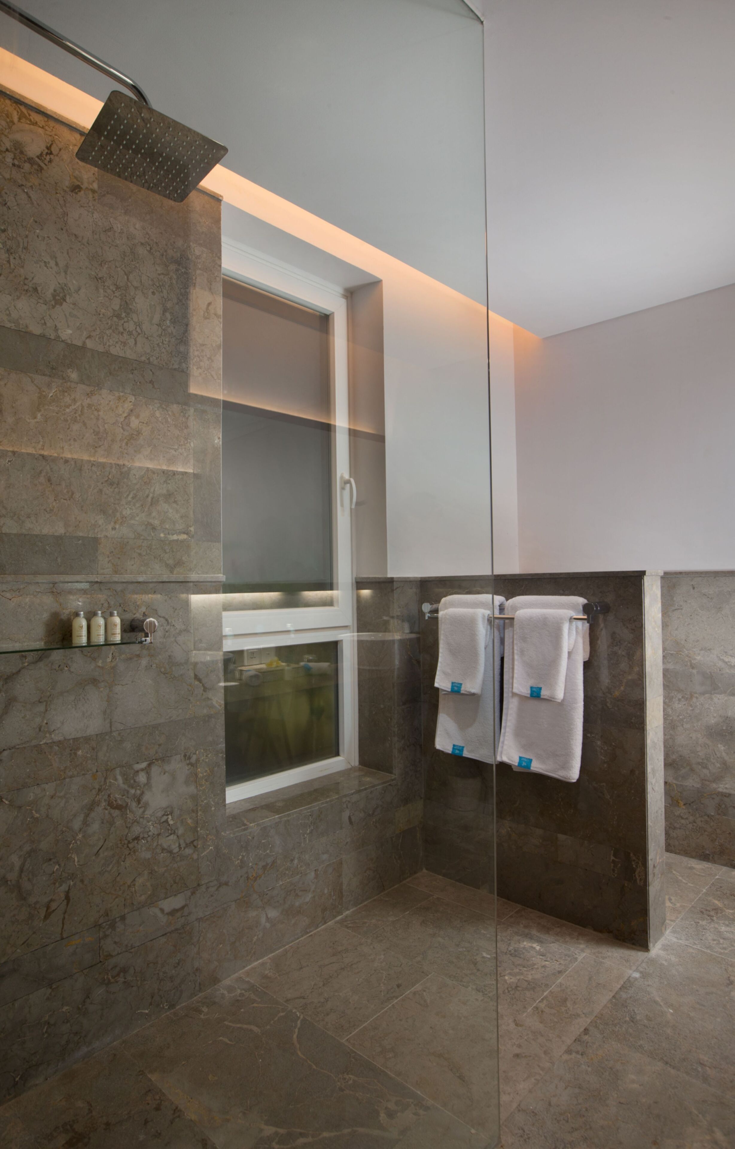 Un baño moderno con cabina de ducha de vidrio, paredes de mármol y puerta de vidrio que da acceso a la zona de ducha.