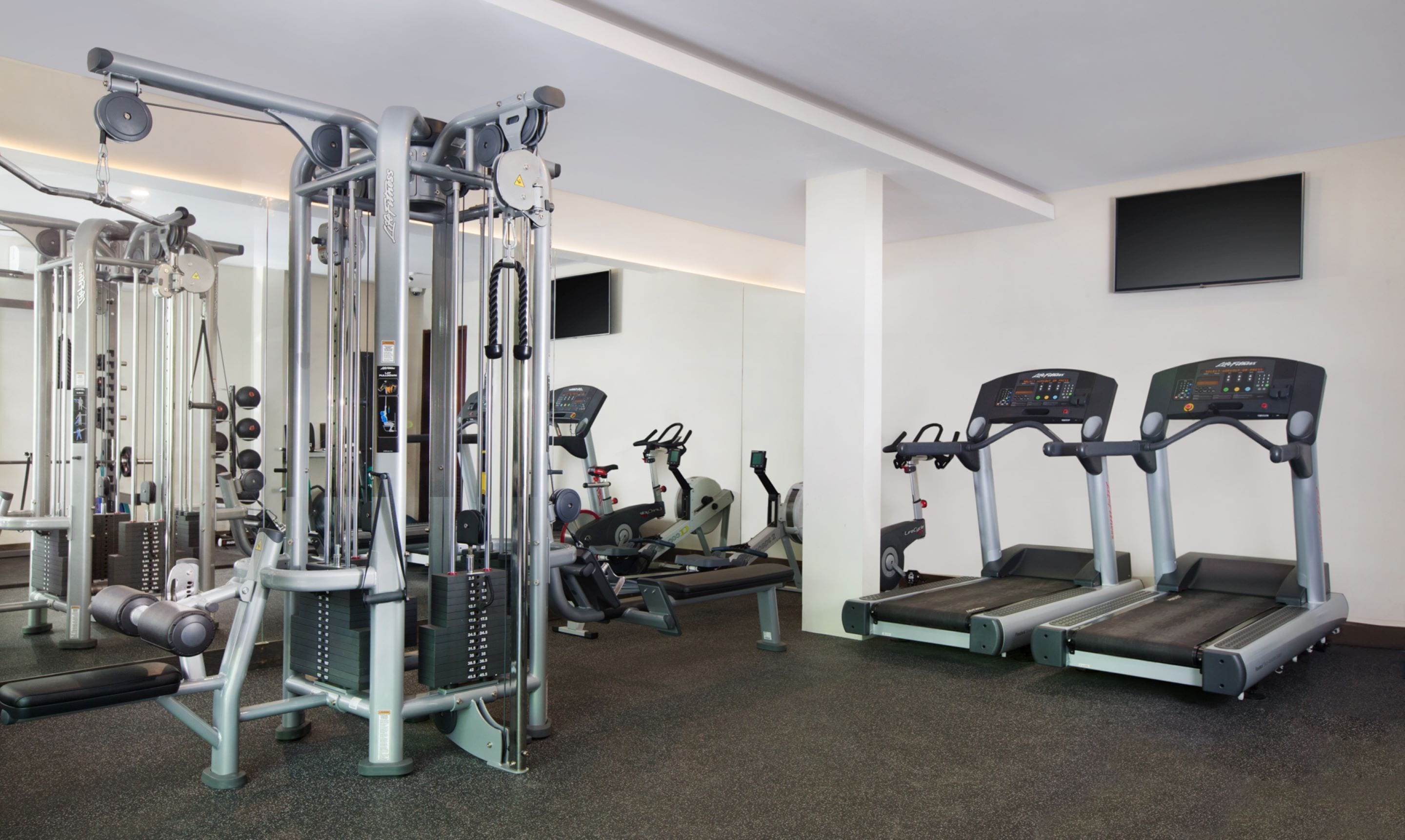 Un gimnasio con diversos equipos de ejercicio, incluyendo una máquina de poleas, cintas de correr y bancos de pesas.