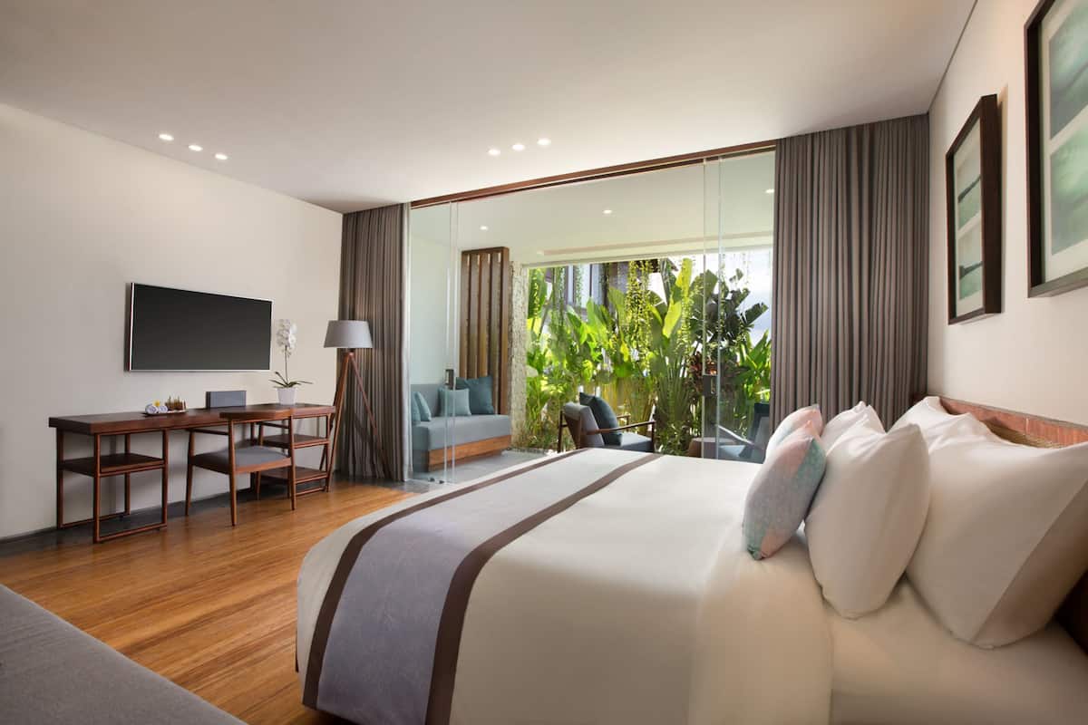 Une chambre d’hôtel moderne, dotée d’un grand lit, d’un bureau, d’un canapé et d’une grande fenêtre avec des rideaux.