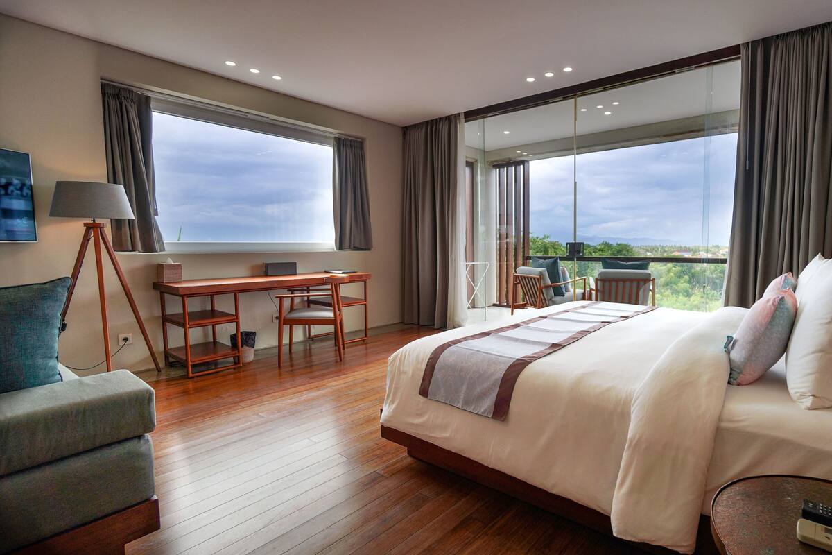 Une chambre d’hôtel avec un grand lit, un bureau, une chaise et une vue sur l’extérieur.