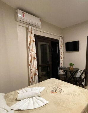 A hotel room with a bed, a table, a chair, an air conditioning unit, and a television on the wall.