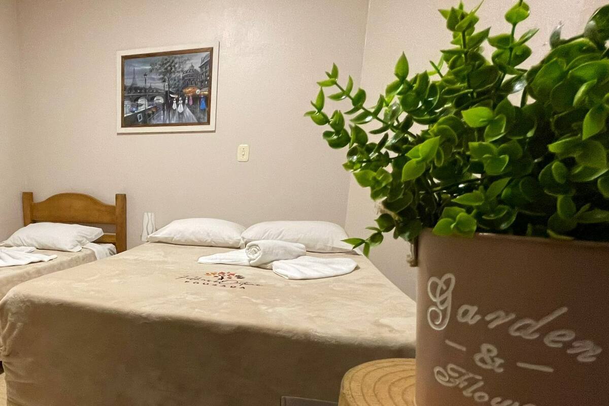 Ein Hotelzimmer mit zwei Betten, einem gerahmten Bild an der Wand und einer Topfpflanze mit der Aufschrift 'Garden & Flower'.
