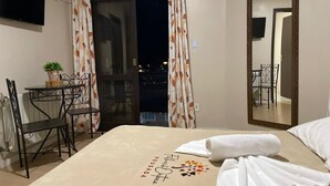 Habitación de hotel con cama, escritorio, silla, planta en maceta y puerta al balcón.