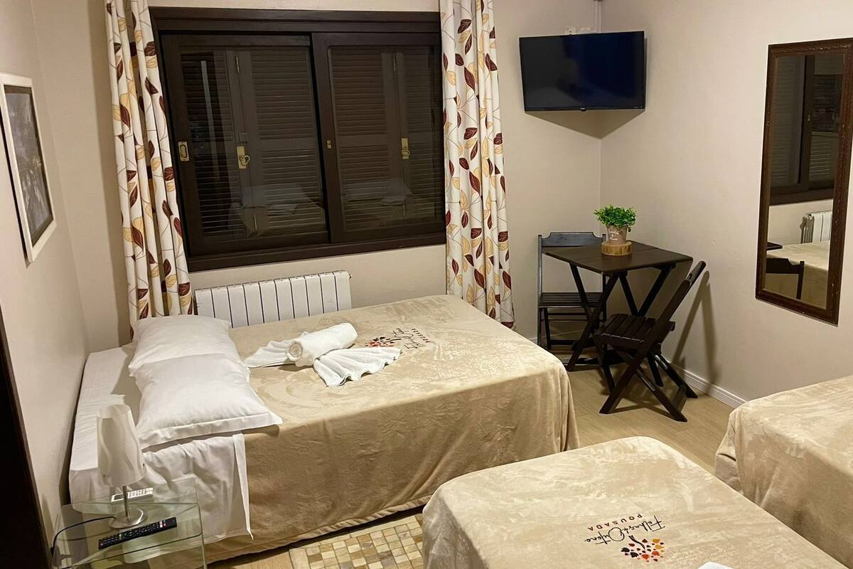 Ein Hotelzimmer mit zwei Betten, einem kleinen Tisch, einem Stuhl, einem Fernseher und einem Spiegel.