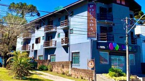 Un edificio de varios pisos con un llamativo letrero que dice 'Pousada', balcones y un escaparate con señalización colorida.