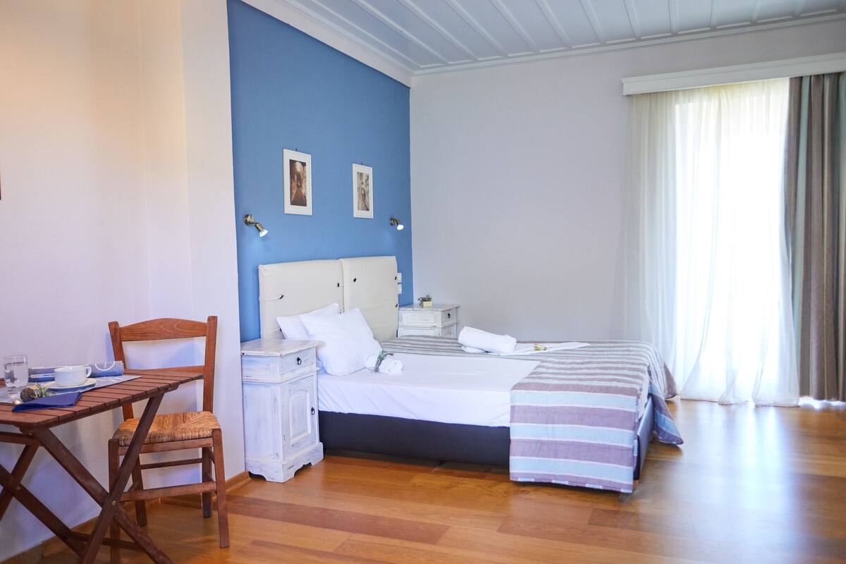 A bedroom with a bed, a chair, a small table, and a nightstand.