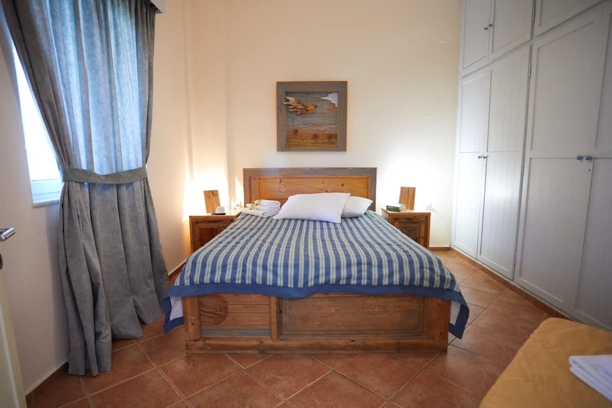 A bedroom with a wooden bed, a nightstand, a bedside table, a wardrobe, and a window with curtains.