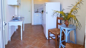 Une cuisine compacte avec un réfrigérateur blanc, une table à manger avec des chaises et une petite table bleue ornée d’un vase rempli de fleurs jaunes.
