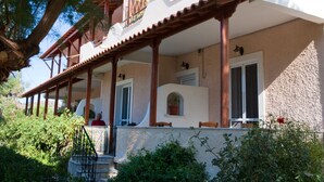 Une maison traditionnelle de style méditerranéen, dotée d’une façade en pierre, d’un balcon en bois et d’une végétation luxuriante qui entoure la propriété.