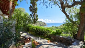 Un sentier de pierres mène à un point de vue sur la côte, avec un bâtiment rustique et une végétation luxuriante.