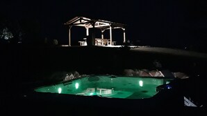 Ein Blick auf einen Poolbereich bei Nacht, mit einer Laube und einem Whirlpool.