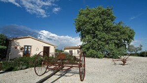 Ein rustikales Gebäude mit einem großen Baum davor, einem alten Wagen und Kiesstreuung.