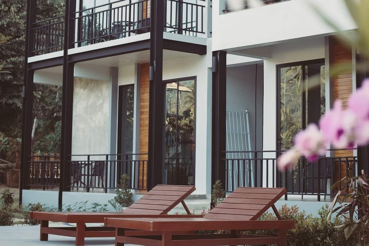 A modern two-story building with a swimming pool, lounge chairs, and a balcony.
