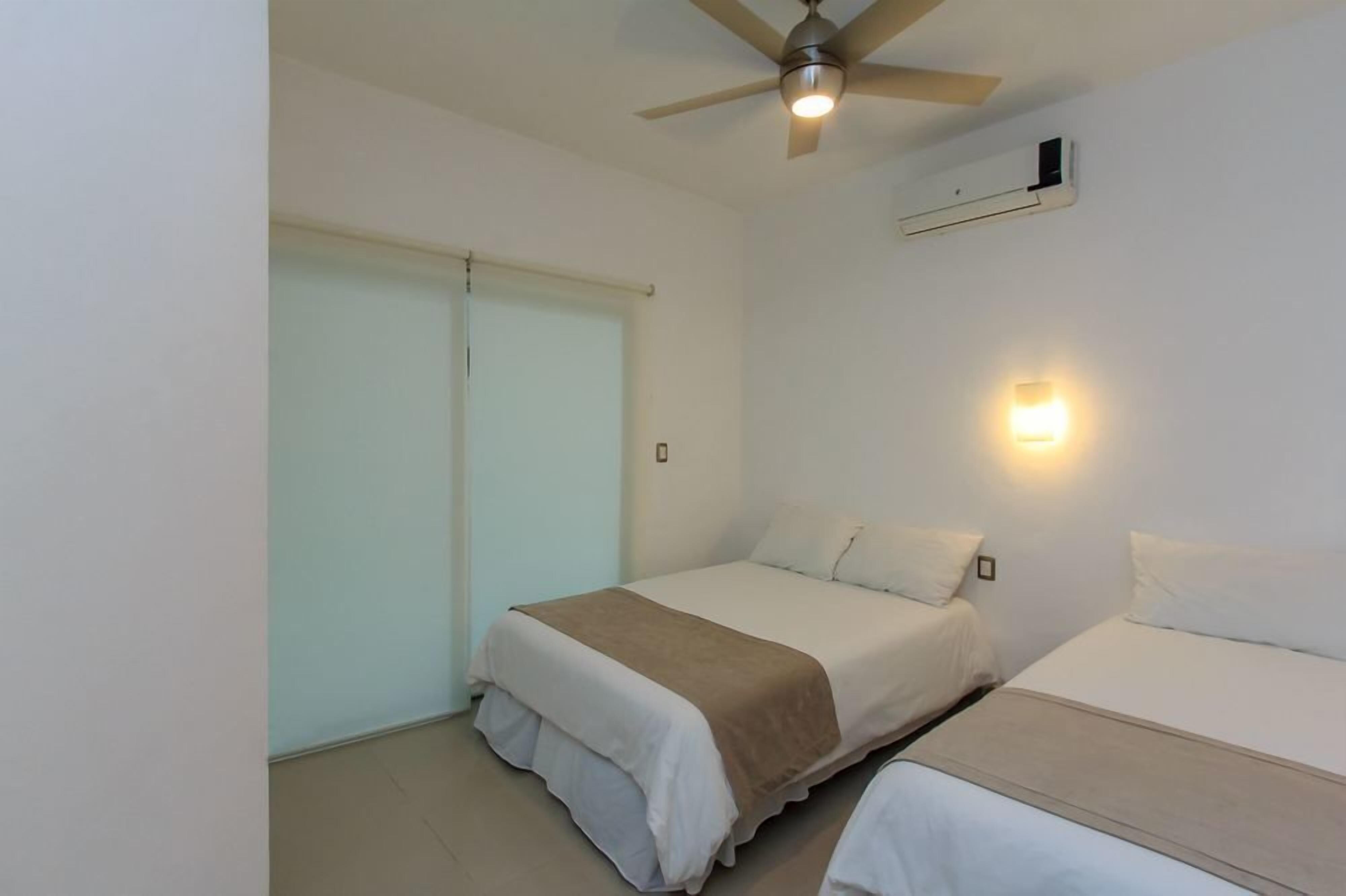 A bedroom with two beds, a ceiling fan, an air conditioning unit, and a window with a blind.