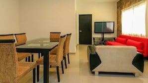 A modern living room with a glass-top dining table, wicker chairs, a red sofa, and a flat-screen TV. - Davinci By Vtpvacaciones (Playa del Carmen)