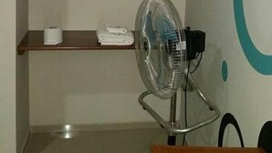 A room with a wooden shelf, a fan, and a wall with a circular design. - Hospedaje Piolin (Tarapoto)