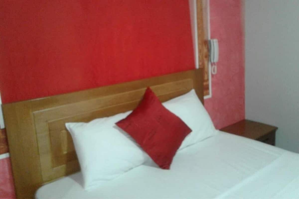 A bed with white and red pillows, a wooden headboard, and a nightstand with a lamp.