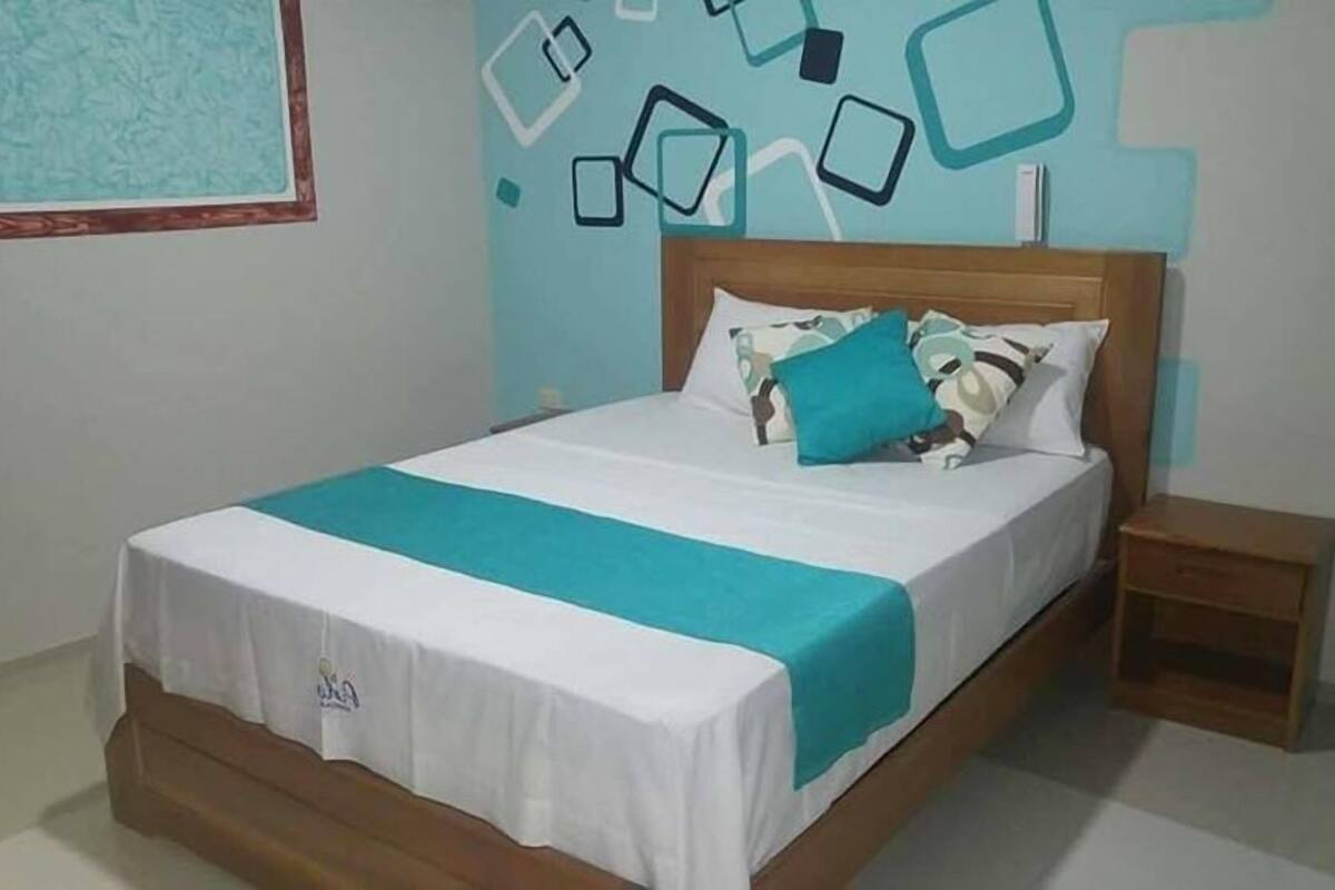 A neatly made bed with a white and teal bedspread, a wooden headboard, and a small bedside table.