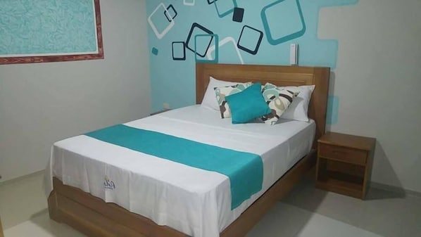 A neatly made bed with a white and teal bedspread, a wooden headboard, and a small bedside table.