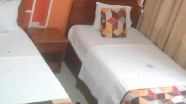 A hotel room with two beds, a wooden headboard, a telephone, and a window with curtains. - Hospedaje Piolin (Tarapoto)