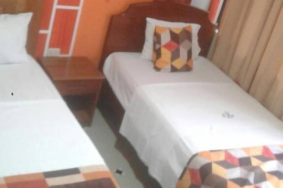A hotel room with two beds, a wooden headboard, a telephone, and a window with curtains.