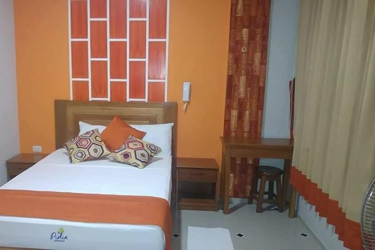 A hotel room with a bed, a wooden nightstand, a desk, and a chair.