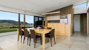 Une cuisine moderne dotée d’un grand îlot central, d’un coin repas avec une table et des chaises, et offrant une vue sur la campagne.
