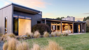 Une maison moderne dotée de grandes fenêtres en verre, d’une cheminée en pierre et d’une pelouse bien entretenue.
