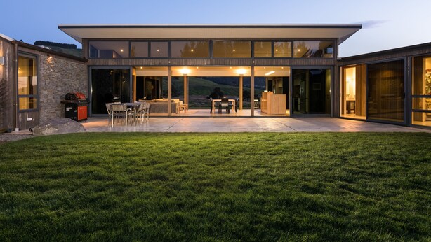 Une maison moderne dotée d’un vaste patio, de grandes fenêtres et d’une pelouse bien entretenue.