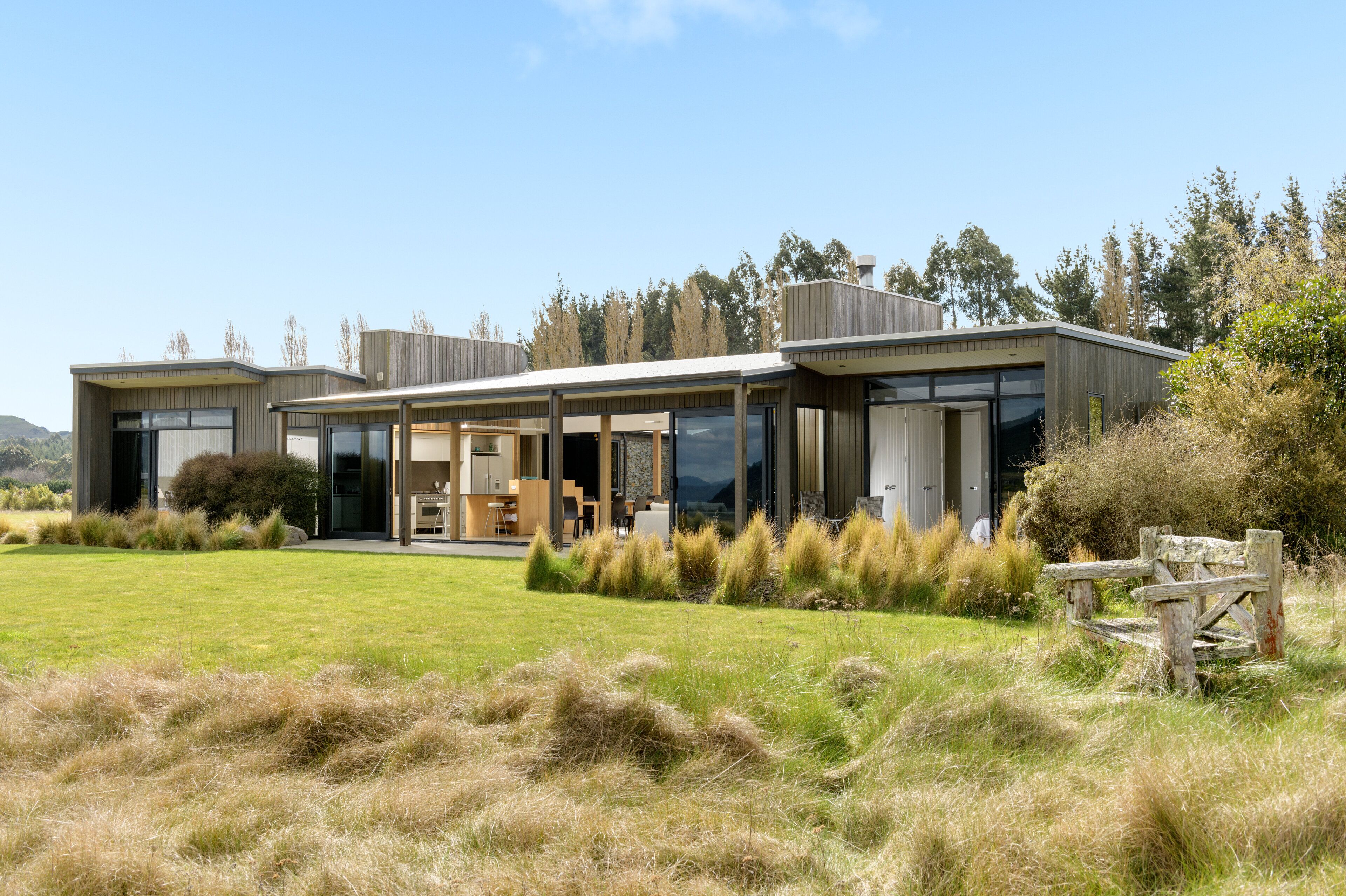 Een modern huis met grote raampartijen, een houten terras en een gazon.