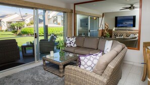 A modern living room with a glass sliding door leading to a patio, a comfortable sofa, a coffee table, and a flat-screen TV mounted on the wall.