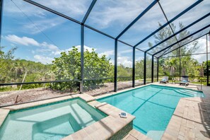 An outdoor swimming pool with a glass enclosure, surrounded by lounge chairs and a view of the surrounding greenery.