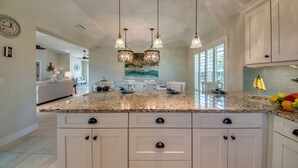 A kitchen with white cabinets, granite countertops, and pendant lighting.