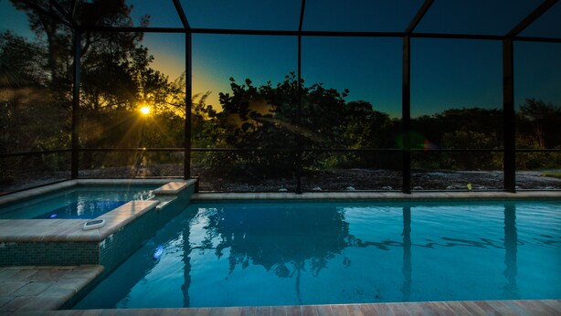 A swimming pool with a view of trees and the sunset.