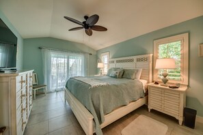 A bedroom with a bed, a dresser, a nightstand, a ceiling fan, and a window with curtains.