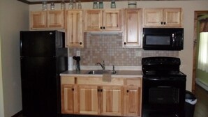 Una cocina compacta con armarios de madera, un refrigerador negro, un microondas y una estufa.