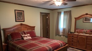 Un dormitorio con cama de madera, ventilador de techo, cómoda y un cuadro en la pared.