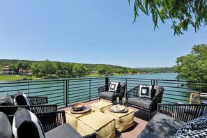 An outdoor seating area with wicker furniture, a table with a bowl and glasses, and a view of a lake and greenery.