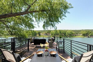 An outdoor deck with a view of a lake, furnished with chairs and tables, and a railing. - Minutes to Downtown Austin: Peaceful Waterfront Retreat with City Access Nearby (Austin)