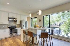 A modern kitchen with a central island, bar stools, and large windows offering a view of the outdoors.