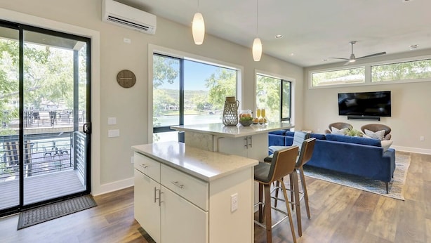 Una cocina moderna con una isla central, un comedor con taburetes de bar, un sofá azul y un televisor en la pared.