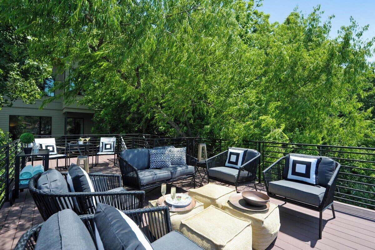 An outdoor patio with wicker furniture, a dining table, and a view of lush greenery.