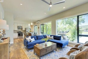 Un vaste espace de vie agrémenté d’un canapé bleu, d’une table basse en bois et offrant une vue sur l’extérieur grâce à de grandes fenêtres.