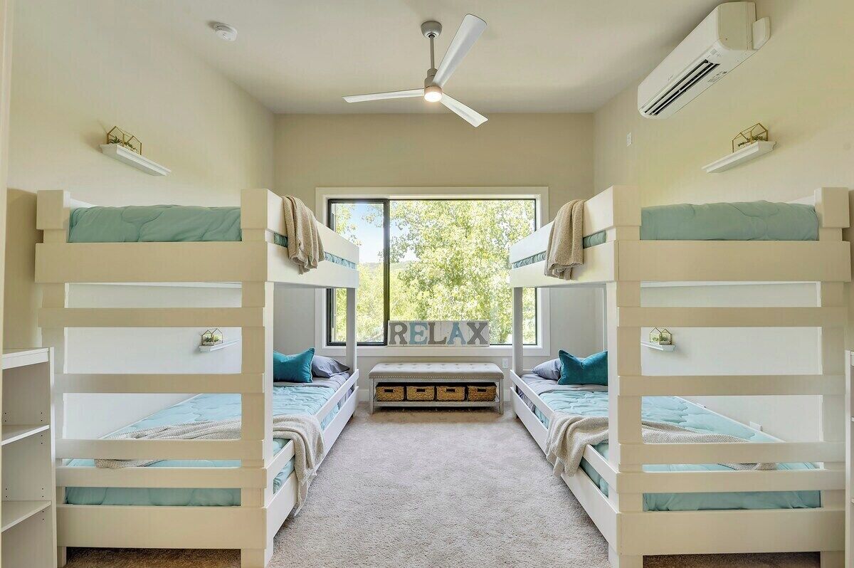 A room with bunk beds, a ceiling fan, an air conditioning unit, and a window with a view of trees.